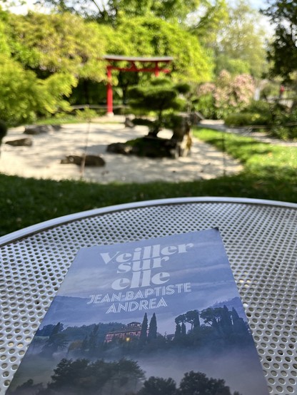 Un livre, Veiller sur elle de JeanBaptiste Andea, posé sur une table de jardin blanche, face à un jardin japonais, sable et verdure
