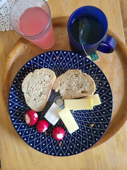 Un verre de sirop de rhubarbe, une tasse de tisane, une assiette avec pain, fromage, radis